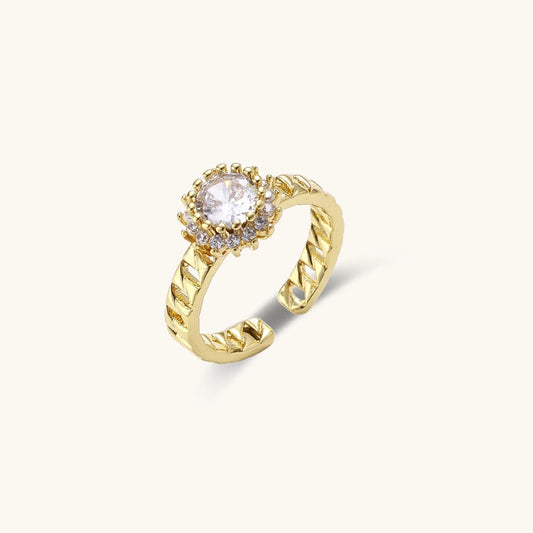 Gold-plated adjustable ring with twisted chain band, central cubic zirconia stone surrounded by crystal halo on cream background