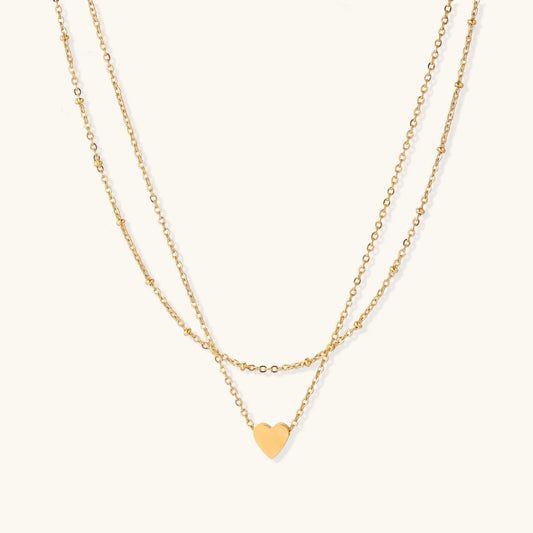 Delicate double-chain gold necklace with tiny heart pendant on cream background