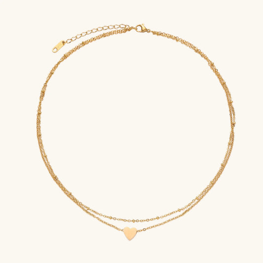 Delicate double-chain gold necklace with tiny heart pendant on cream background